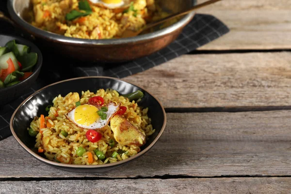Tasty rice with meat, egg and vegetables in bowl served on wooden table. Space for text