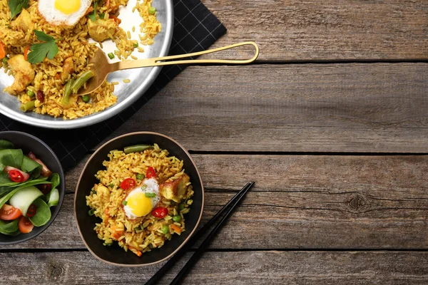 Tasty rice with meat, egg and vegetables in bowl served on wooden table, flat lay. Space for text