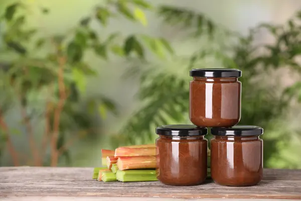 Jars of tasty rhubarb jam and stalks on wooden table. Space for text