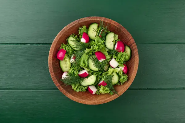 Delicious salad with radish, lettuce, dill and cucumber on green wooden table, top view