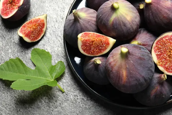 Whole and cut ripe figs with leaf on light grey textured table, flat lay