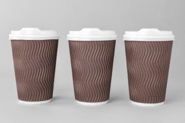 Açık gri arka planda beyaz kapaklı kağıt bardaklar. Kahve hazır.