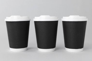 Açık gri arka planda beyaz kapaklı kağıt bardaklar. Kahve hazır.