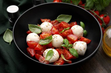Domatesli Caprese salatası, mozzarella topları ve ahşap masada fesleğen, yakın plan.