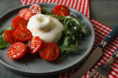 Gri ahşap masada servis edilen domatesli ve roka soslu lezzetli burata peyniri.