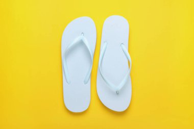 Sarı arka planda şık beyaz parmak arası terlikler, üst görünüm