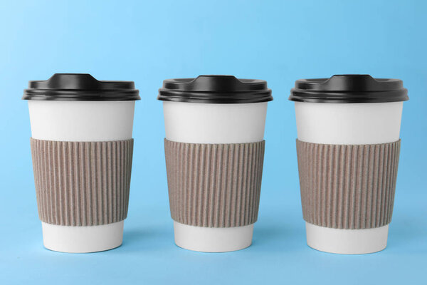 Paper cups with black lids on light blue background. Coffee to go