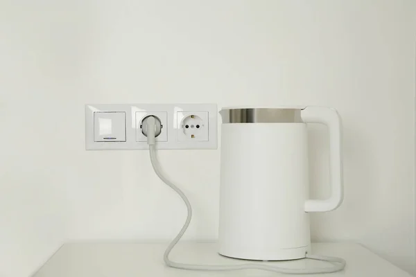 Electric kettle plugged into power socket on white wall