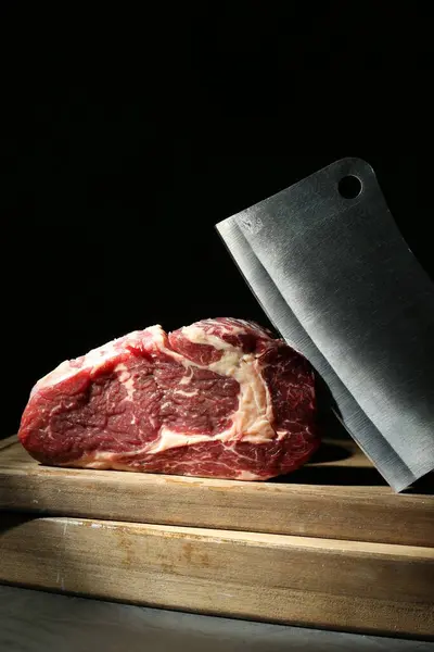 Piece of raw beef meat and knife on grey table against black background