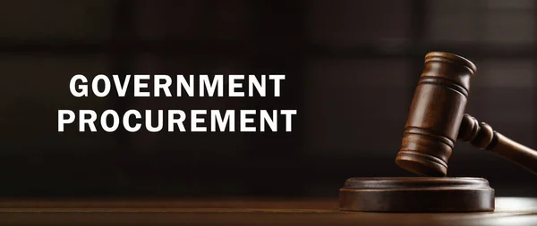 Government procurement. Wooden gavel on table and text against blurred background, banner design