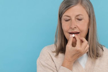 Kıdemli kadın açık mavi arka planda hap alıyor. Metin için boşluk