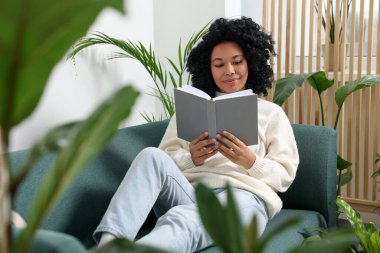 Rahatlatıcı atmosfer. Kanepede kitap okuyan bir kadın. Etrafı güzel çiçeklerle çevrili.