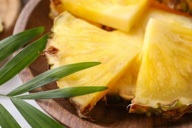 Lezzetli olgun ananas parçaları kasede ve yeşil yapraklar, yakından.