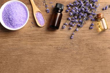 Bir kase deniz tuzu, temel yağ ve lavanta çiçekleri ahşap masada, düz yerde. Metin için boşluk