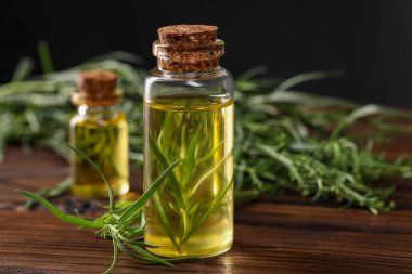 Kaliteli yağ şişeleri ve taze tarhun yaprakları ahşap masada, yakın plan. Metin için boşluk