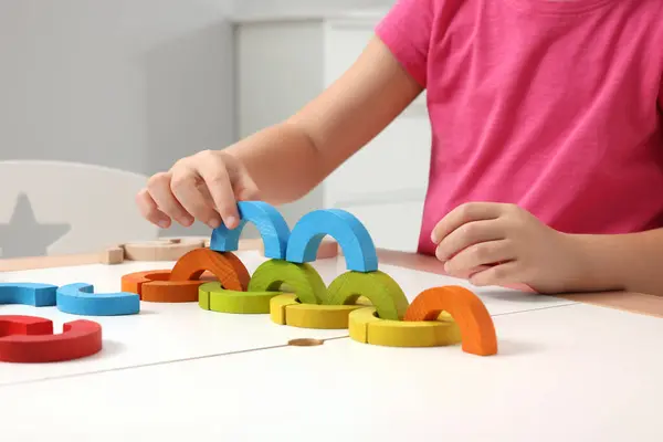 Motor skills development. Girl playing with colorful wooden arcs at white table indoors, closeup