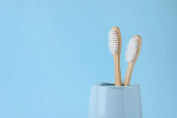 Bamboo toothbrushes in holder on light blue background, space for text