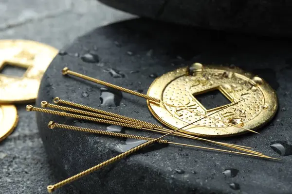 Akupunktur iğneleri, antik madeni para ve taş, gri desenli masaya su damlaları, yakın plan.