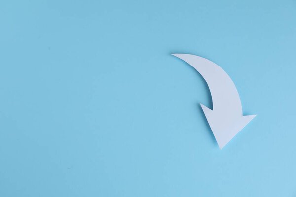 White curved paper arrow on light blue background, top view. Space for text