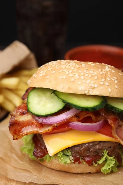 Tasty burger with bacon, vegetables and patty on parchment paper, closeup