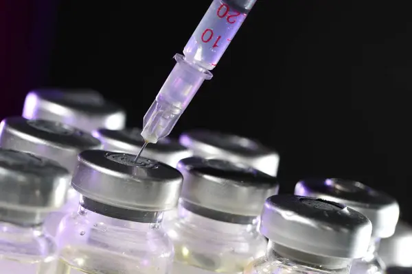 Filling syringe with medicine from vial against dark background, closeup