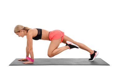 Beyaz arkaplana karşı fitness minderi üzerinde elastik direnç bandıyla egzersiz yapan kadın