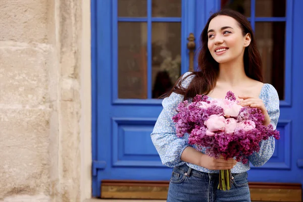 Baharda çiçek buketi olan güzel bir kadın açık hava binasının yanında, yazı yazmak için yer var.