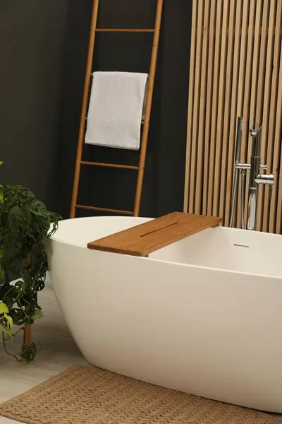 Spa day. Stylish bathroom interior with ceramic tub and green houseplant