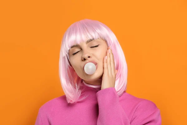 Beautiful woman blowing bubble gum on orange background