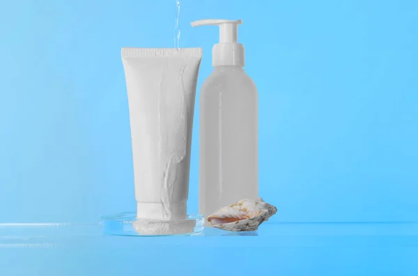 Pouring water on face cleansing products, petri dish and seashell against light blue background