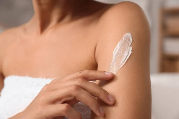 Woman applying body cream onto arm indoors, closeup