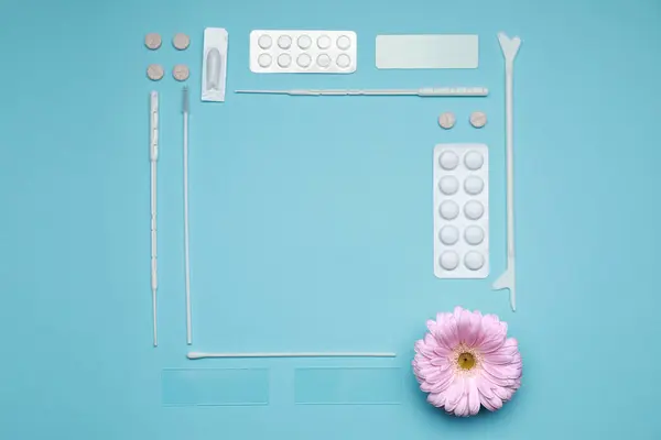 Frame of many gynecological pills, tools and gerbera flower on light blue background, flat lay. Space for text