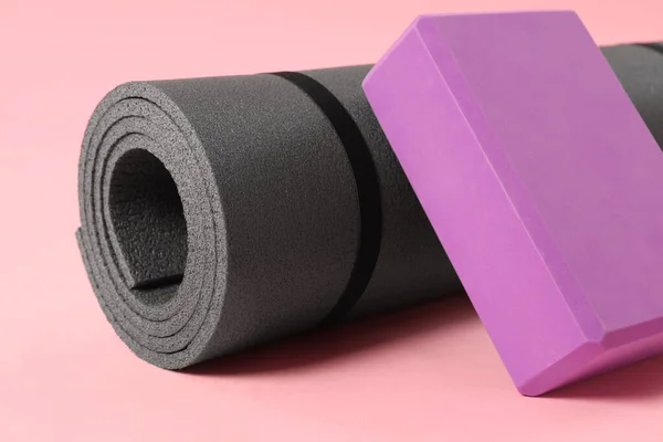 Grey exercise mat and yoga block on pink background, closeup