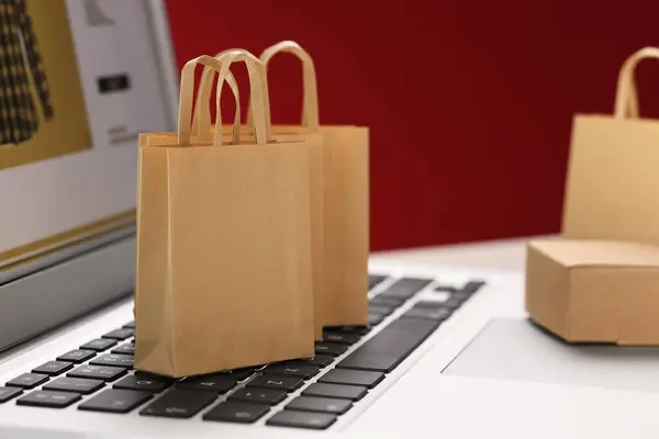 Mini shopping bags on laptop against red background, closeup. Online store
