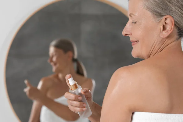 Happy woman applying body oil onto shoulder near mirror indoors. Space for text