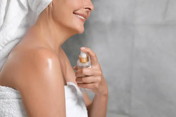 Happy woman applying body oil onto shoulder near grey wall, closeup. Space for text