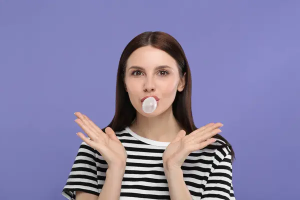 Beautiful woman blowing bubble gum on light purple background, space for text