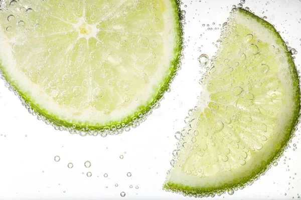 Juicy lime slices in soda water against white background, closeup