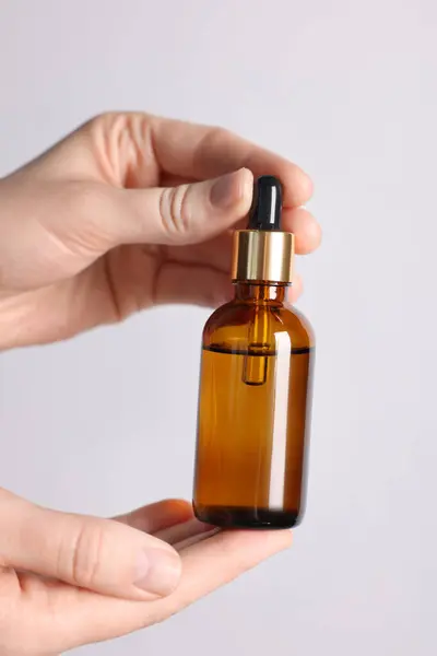 Woman holding bottle of cosmetic oil on light background, closeup