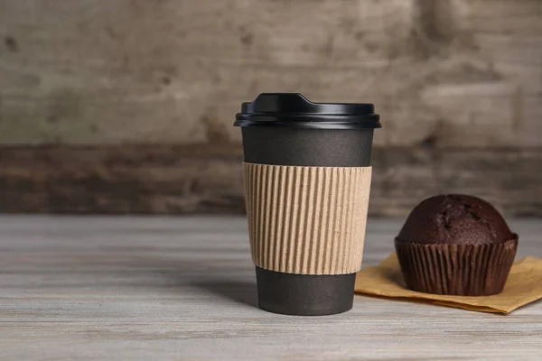 Paper cup with black lid and muffin on wooden table, space for text. Coffee to go