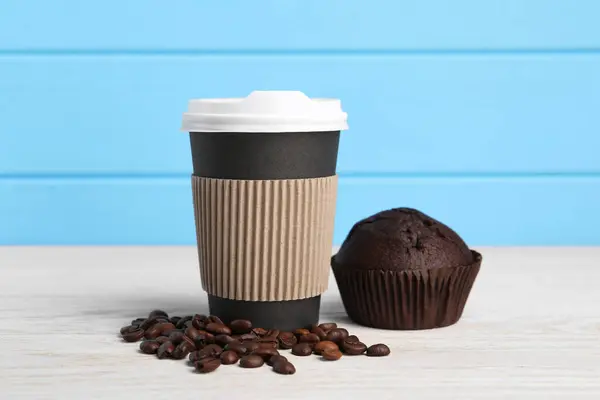Paper cup with plastic lid, coffee beans and muffin on white wooden table. Coffee to go