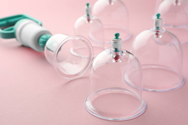 Пластиковые чашки и ручной насос на розовом фоне, крупным планом. Терапия