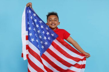 4 Temmuz - ABD 'nin Bağımsızlık Günü. Açık mavi arka planda Amerikan bayrağı taşıyan mutlu çocuk