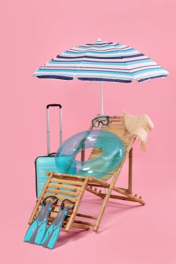Güverte sandalyesi, bavul ve pembe arka planda plaj aksesuarları.
