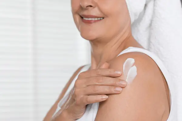 Happy woman applying body cream onto shoulder indoors, closeup. Space for text