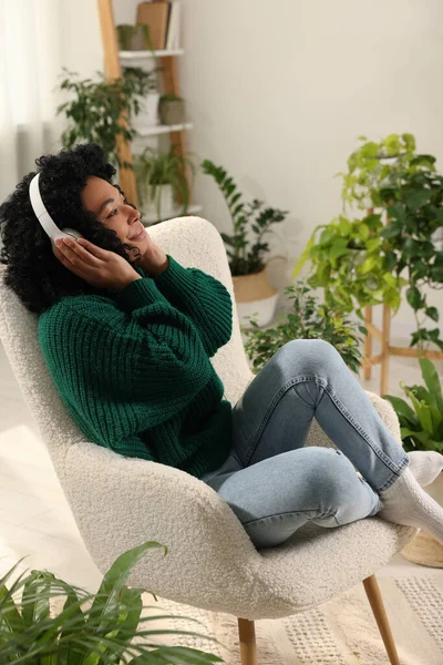 Relaxing atmosphere. Woman wearing headphones and listening music in room with beautiful houseplants