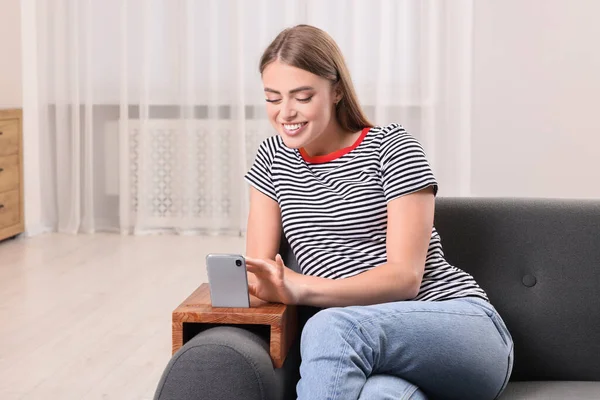 Happy woman using smartphone on sofa armrest wooden table at home, space for text