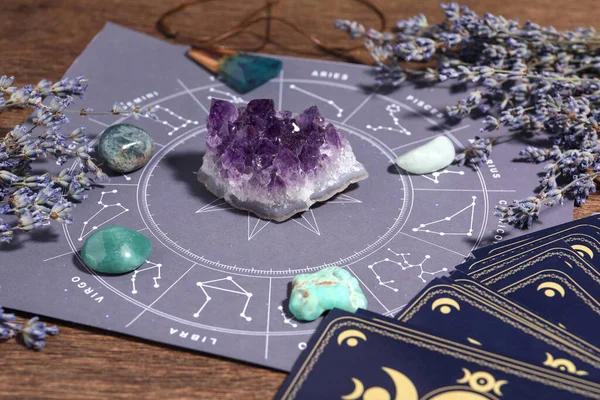 Astrology prediction. Zodiac wheel, gemstones, tarot cards and lavender on wooden table, closeup