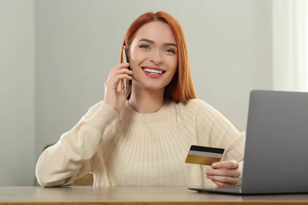 Happy woman with credit card using smartphone for online shopping at wooden table indoors