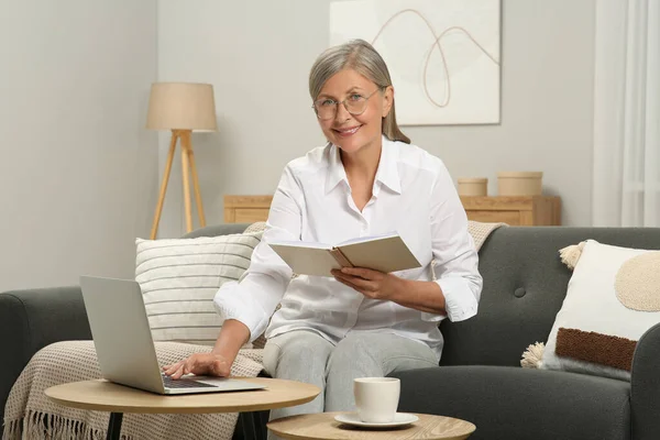 Beautiful senior woman with notebook using laptop at home